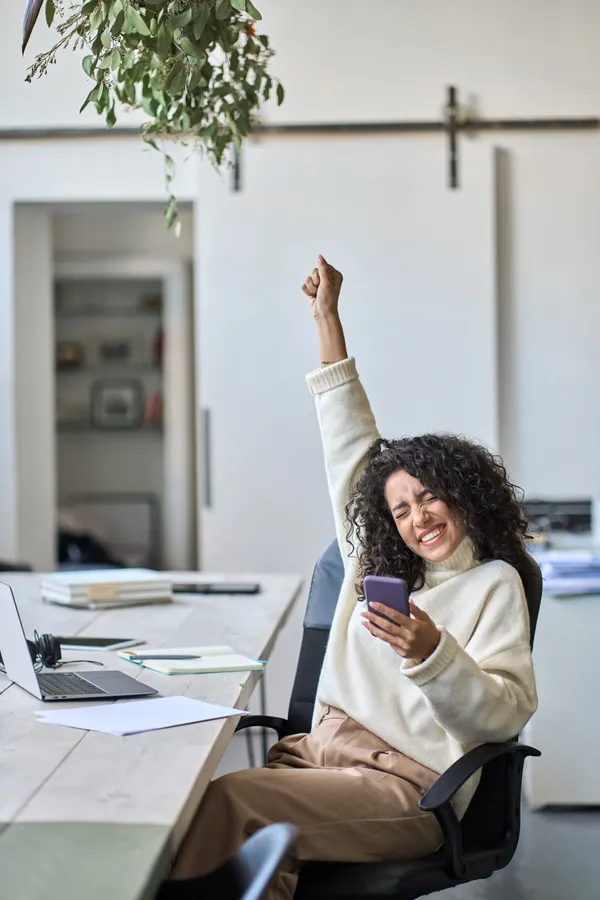Euphoric young female worker holding mobile phone celebrating win